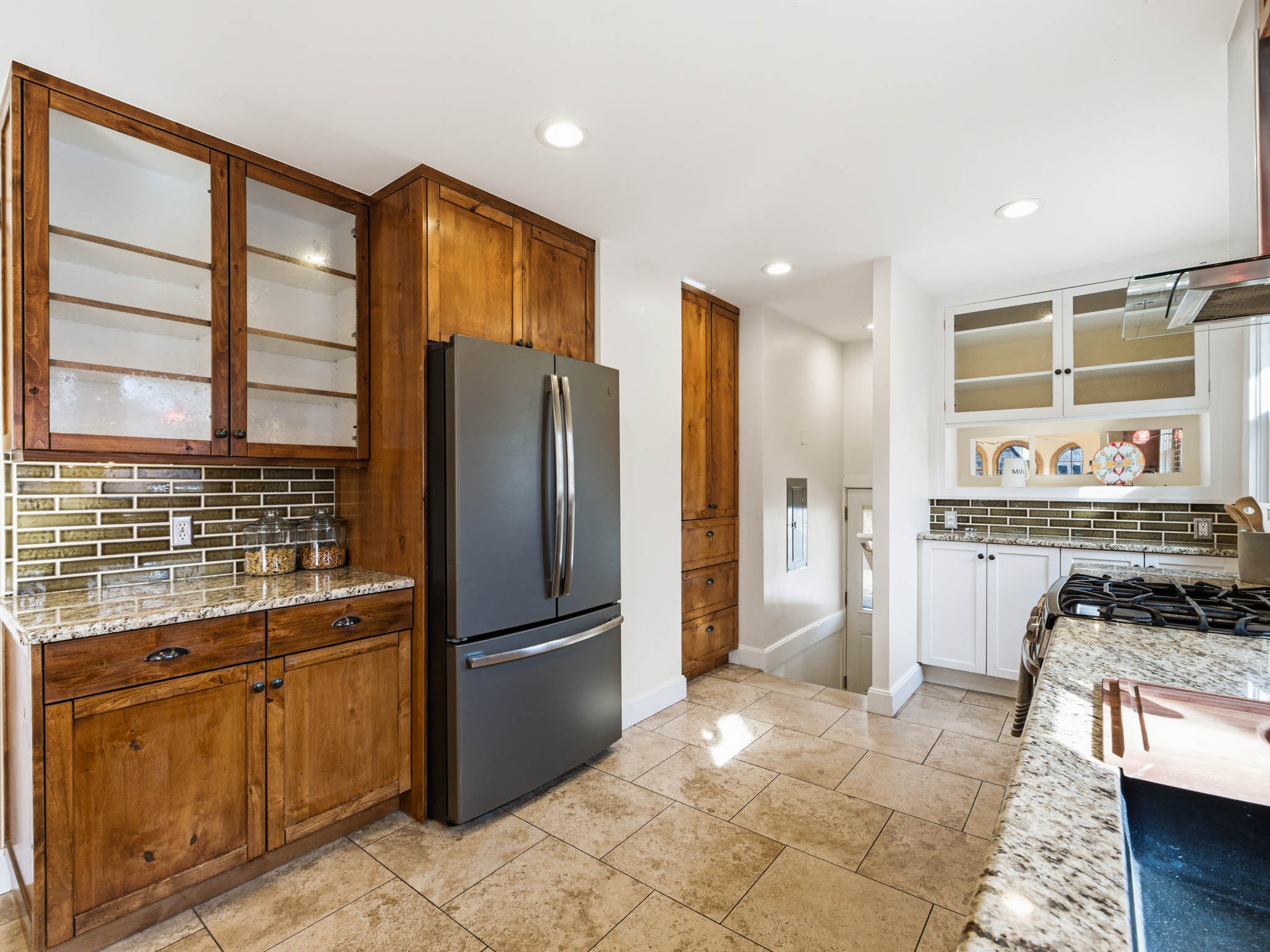 Kitchen with glass fronted cabinets, light stone countertops, backsplash, freestanding refrigerator, and range hood