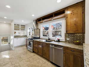 Kitchen with stainless steel appliances, extractor fan, open shelves, light stone countertops, and decorative backsplash