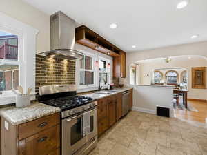 Kitchen with stainless steel appliances, light stone countertops, island range hood, wood finish cabinetry, and recessed lighting