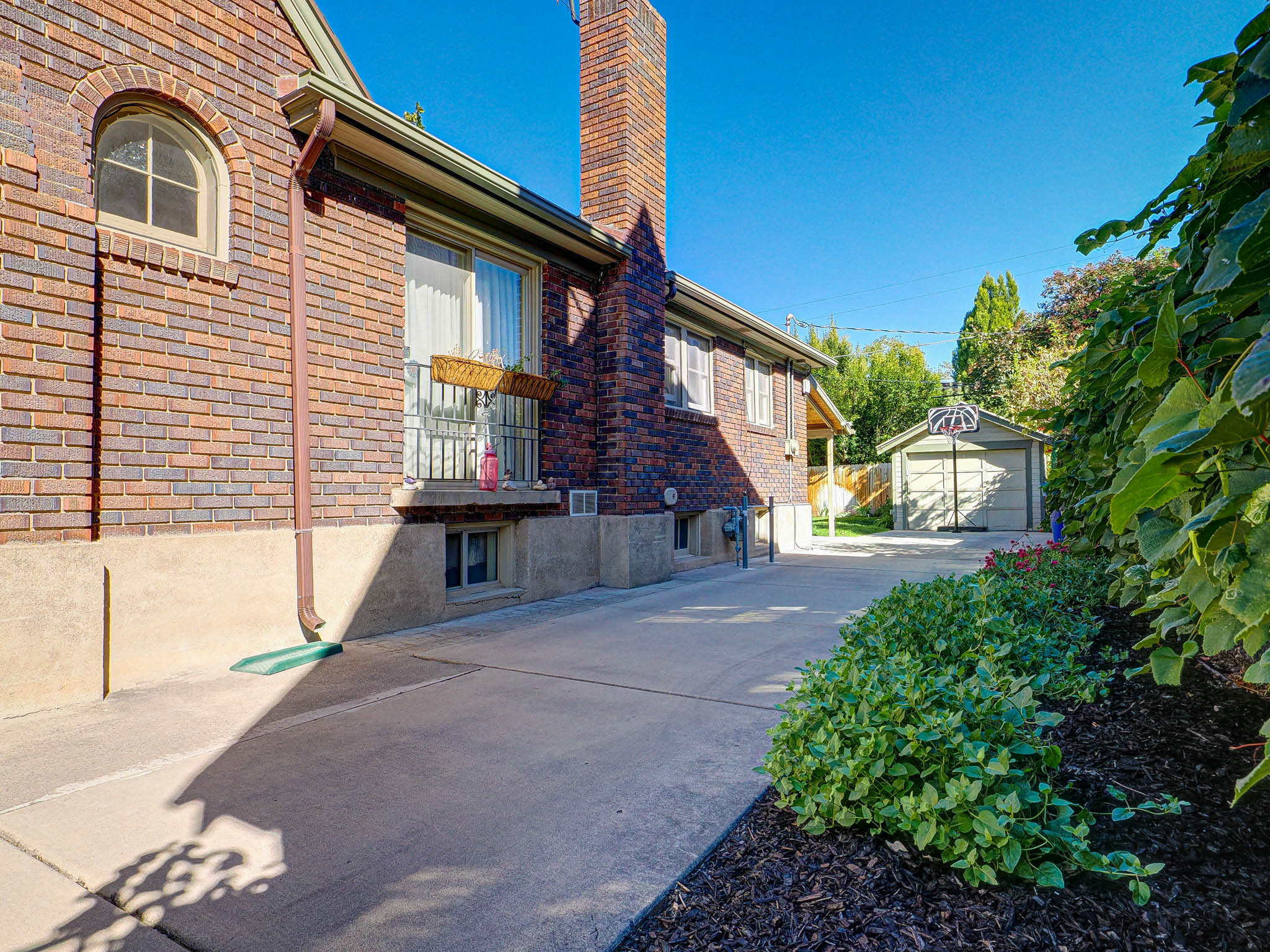 View of property exterior with a garage, a chimney, brick siding, and an outbuilding