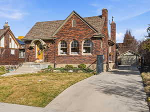 Tudor house with an outbuilding, a front yard, a garage, brick siding, and a chimney