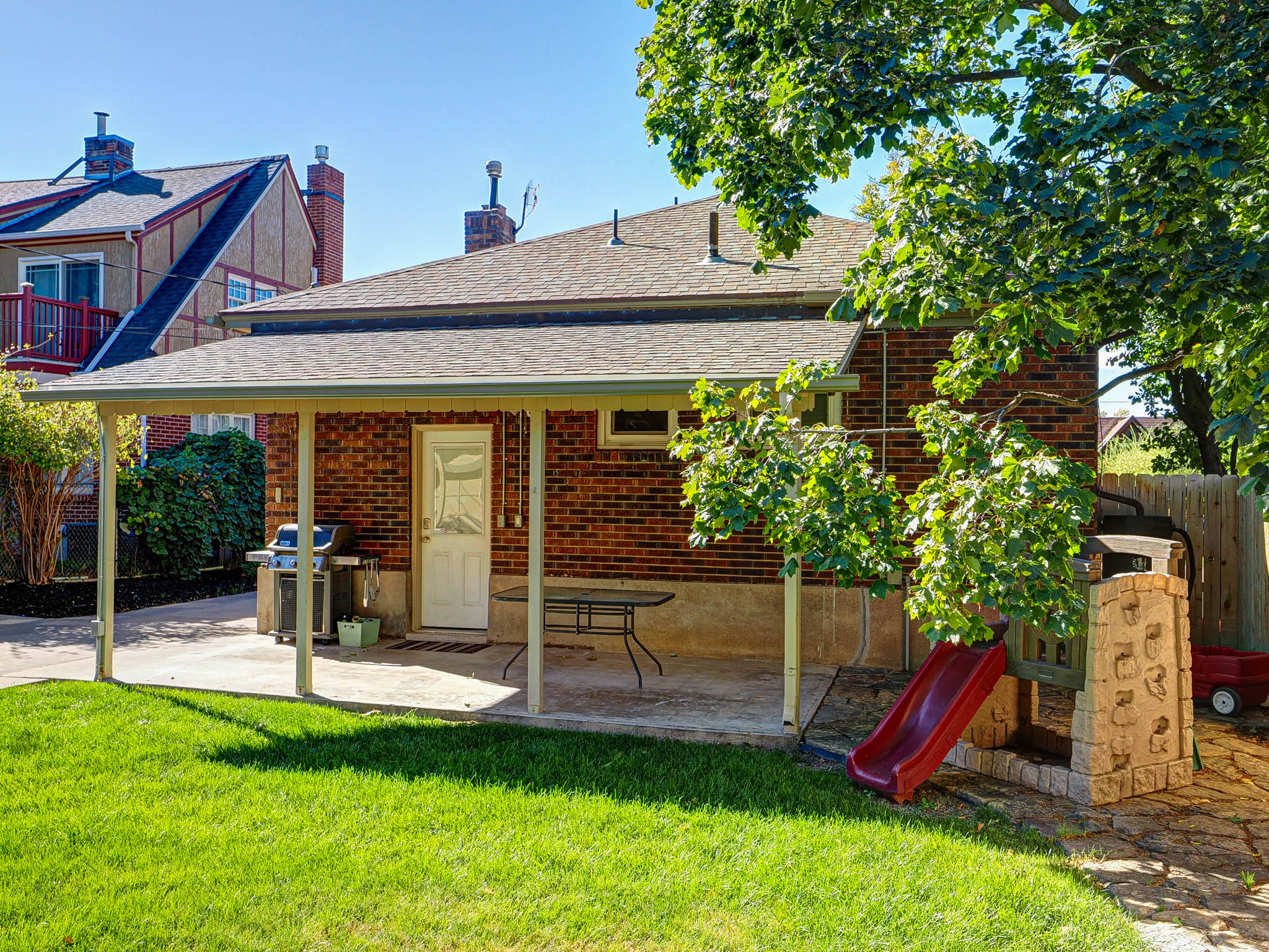 Rear view of house with a shingled roof, brick siding, a chimney, and a playground