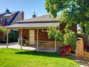 Rear view of house with a shingled roof, brick siding, a chimney, and a playground