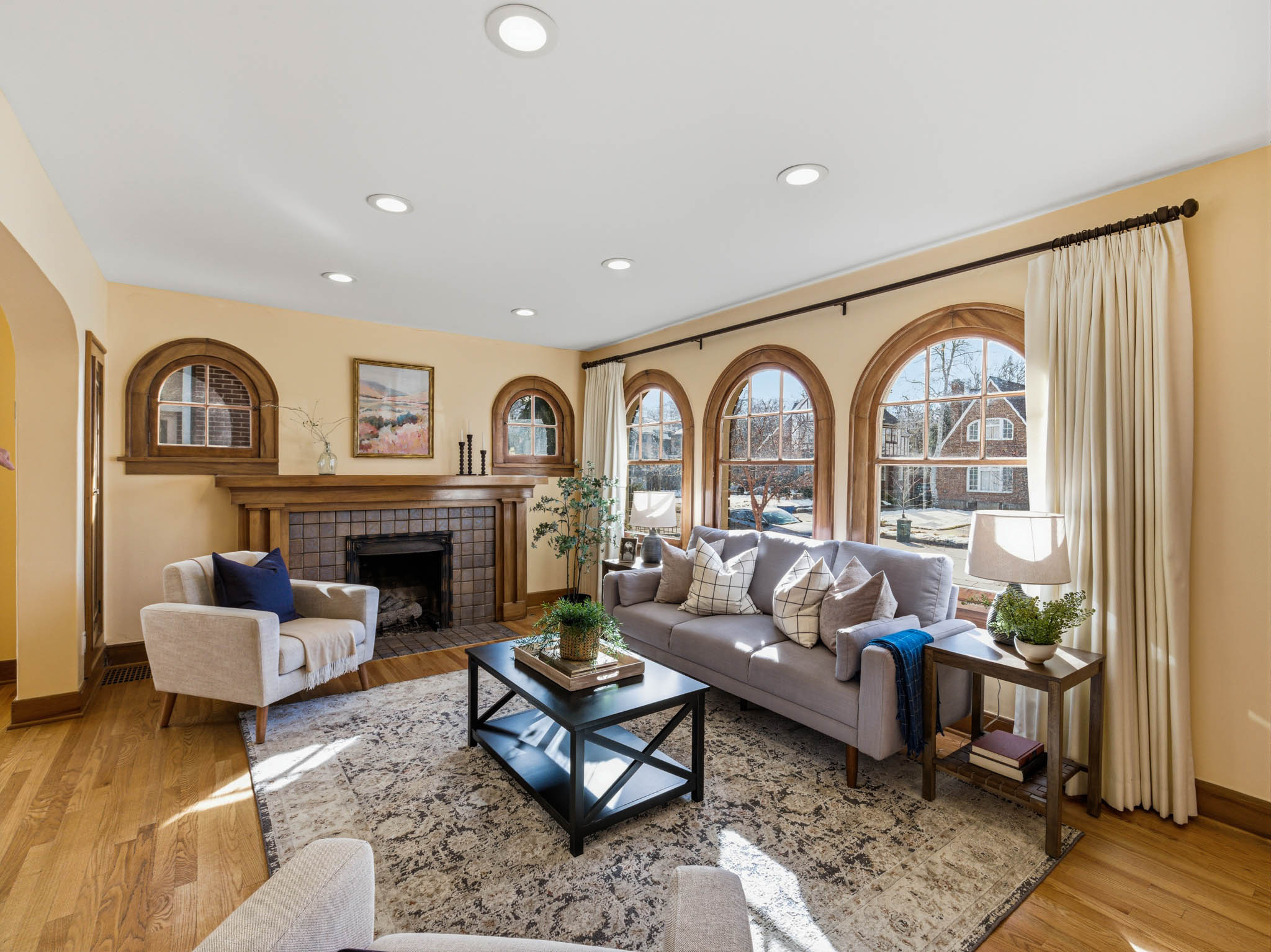 Living room with a tiled fireplace, light wood-style flooring, plenty of natural light, recessed lighting, and arched walkways