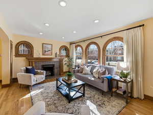 Living room with a tiled fireplace, light wood-style flooring, plenty of natural light, recessed lighting, and arched walkways