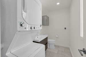 Bathroom with vanity, stacked washer and clothes dryer, light tile patterned flooring, and recessed lighting