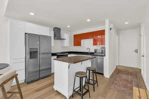 Kitchen featuring stainless steel appliances, a kitchen breakfast bar, white cabinets, light wood-type flooring, and recessed lighting
