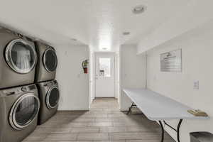 Laundry area featuring a textured ceiling, wood tiled floors, and stacked washer and clothes dryer