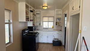Kitchen featuring white cabinets, black electric range oven, light countertops, stainless steel microwave, and light wood finished floors