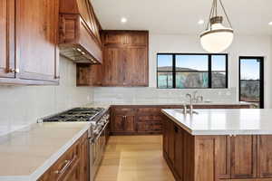 Kitchen featuring range with two ovens, backsplash, pendant lighting, light wood-type flooring, and light stone counters