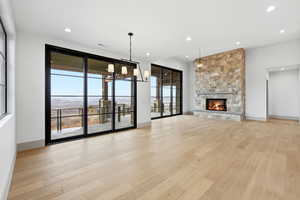 Unfurnished living room with light wood-type flooring, a stone fireplace, and suspended lighting