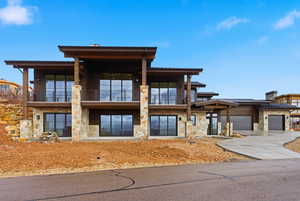 View of front of home featuring stone siding, concrete driveway, an attached garage, and a balcony