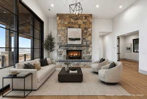 Living room featuring light wood-style floors, a stone fireplace, recessed lighting, and a high ceiling