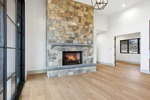 Unfurnished living room with light wood-style flooring, a stone fireplace, and a high ceiling
