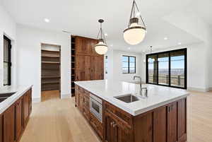 Kitchen featuring light wood-style floors, light stone countertops, a kitchen island with sink, hanging light fixtures, and built in microwave