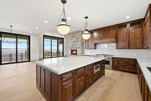Kitchen featuring backsplash, a fireplace, hanging light fixtures, a kitchen island with sink, and light wood-type flooring