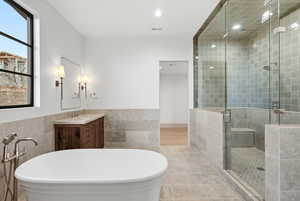Full bathroom with a freestanding tub, tile walls, vanity, a stall shower, and a wainscoted wall