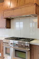 Kitchen featuring double oven range, wood finish cabinets, decorative backsplash, and light stone counters