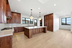 Kitchen featuring tasteful backsplash, a large island, light wood finished floors, hanging light fixtures, and light stone countertops