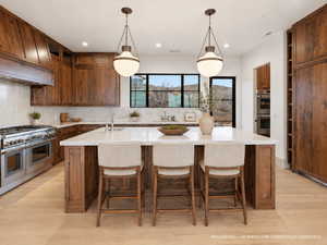 Kitchen featuring a large island with sink, stainless steel appliances, wood finish cabinets, and light wood-style flooring