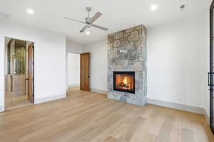 Unfurnished living room featuring light wood-type flooring, ceiling fan, and a stone fireplace