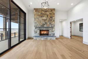 Unfurnished living room featuring a stone fireplace, light wood-style flooring, a high ceiling, and recessed lighting