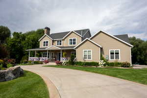 View of front of house with covered porch, a front lawn, a chimney, and driveway