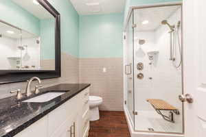 Bathroom featuring tile walls, vanity, a shower stall, wood finish floors, and wainscoting