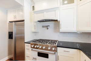 Kitchen featuring premium appliances, white cabinets, dark stone counters, and glass fronted cabinets