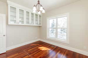 Unfurnished dining area with a chandelier and dark wood-type flooring