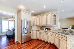 Kitchen featuring stainless steel fridge, light stone countertops, decorative backsplash, hanging lights, and dark wood finished floors