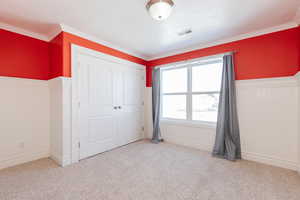 Unfurnished bedroom featuring wainscoting, a closet, crown molding, light carpet, and wooden walls