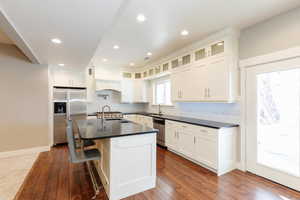 Kitchen with stainless steel appliances, dark wood-style flooring, a kitchen breakfast bar, an island with sink, and dark stone countertops