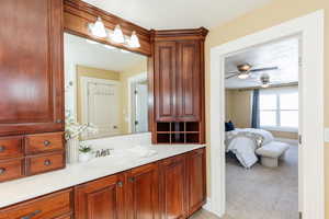 Ensuite bathroom with vanity, light colored carpet, and ceiling fan