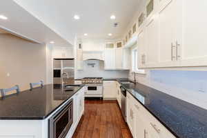 Kitchen featuring dark stone countertops, stainless steel appliances, recessed lighting, glass insert cabinets, and dark wood finished floors