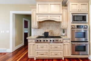 Kitchen with cream cabinetry, stainless steel appliances, light stone countertops, and dark wood-style floors