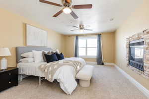 Bedroom featuring a ceiling fan, a fireplace, and light carpet