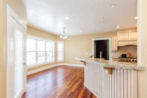 Kitchen with a breakfast bar, light stone countertops, decorative backsplash, dark wood-style floors, and a chandelier