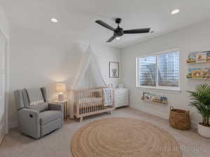 Bedroom with light colored carpet, a nursery area, a ceiling fan, and recessed lighting