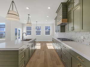 Kitchen featuring light wood-style flooring, decorative light fixtures, two tone cabinets, light stone countertops, and a center island with sink