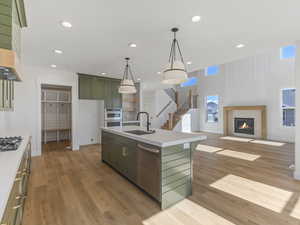 Kitchen with green cabinetry, a tile fireplace, an island with sink, open floor plan, and stainless steel appliances