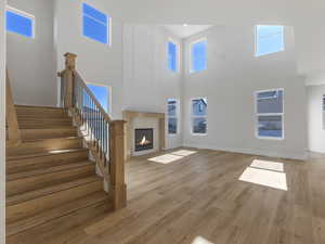 Unfurnished living room featuring a glass covered fireplace, light wood finished floors, and a high ceiling