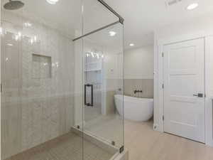 Full bath with a stall shower, a soaking tub, a wainscoted wall, tile walls, and recessed lighting
