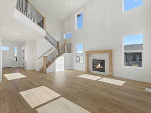Unfurnished living room featuring a fireplace with flush hearth, light wood-type flooring, a high ceiling, and recessed lighting