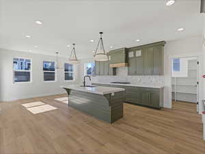 Kitchen featuring green cabinetry, a breakfast bar area, an island with sink, tasteful backsplash, and light wood-style floors