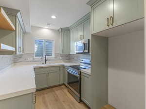 Kitchen with open shelves, stainless steel appliances, light wood-style floors, light stone countertops, and green cabinets