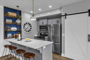 Kitchen featuring gray cabinets, stainless steel appliances, a barn door, and a kitchen bar
