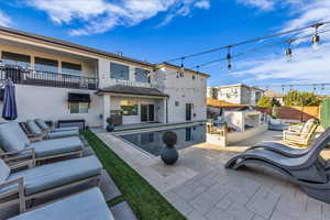 Back of property with stucco siding, an outdoor kitchen with living area, a patio area, a balcony, and a residential view