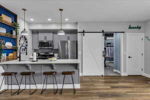 Kitchen with a barn door, stainless steel appliances, light wood-style floors, tasteful backsplash, and a kitchen bar