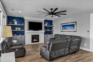 Living area featuring light wood-style flooring, a lit fireplace, a ceiling fan, and built in shelves